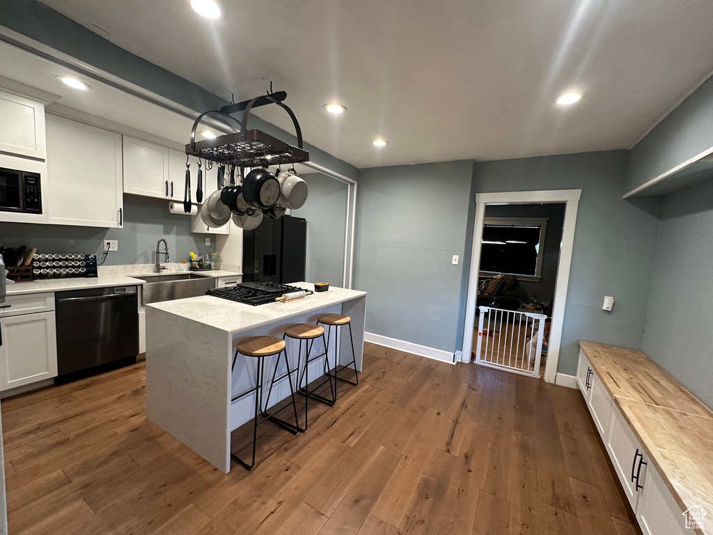 Kitchen featuring black dishwasher, a sink, white cabinetry, recessed lighting, and a kitchen breakfast bar