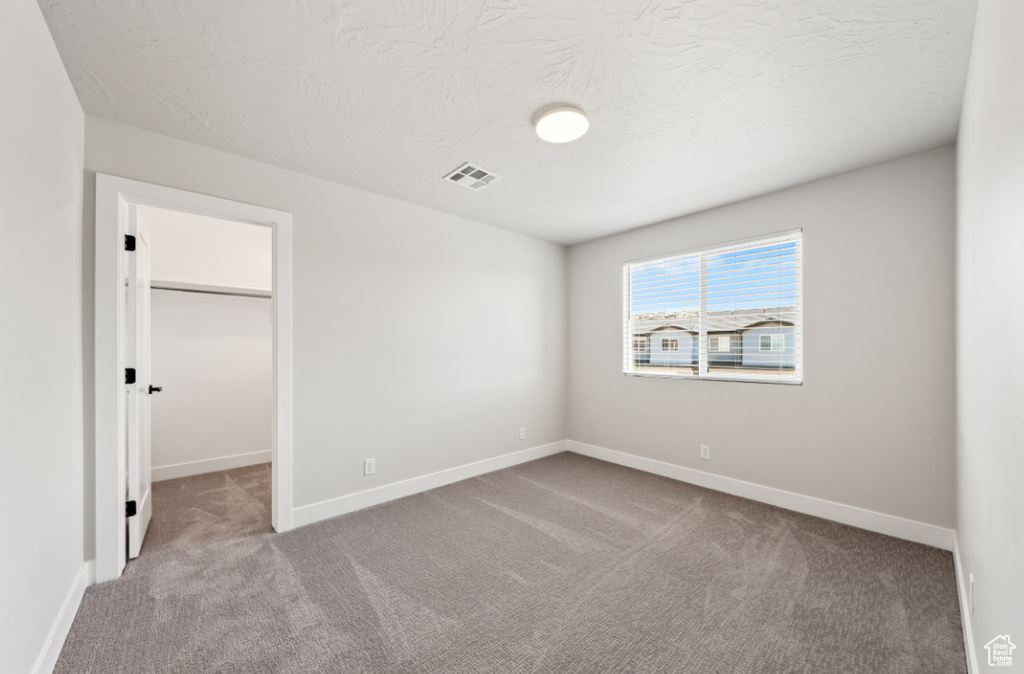 Unfurnished bedroom featuring carpet, a walk in closet, baseboards, a closet, and a textured ceiling