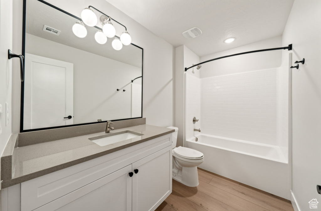 Bathroom with wood finished floors, toilet, vanity, and  shower combination