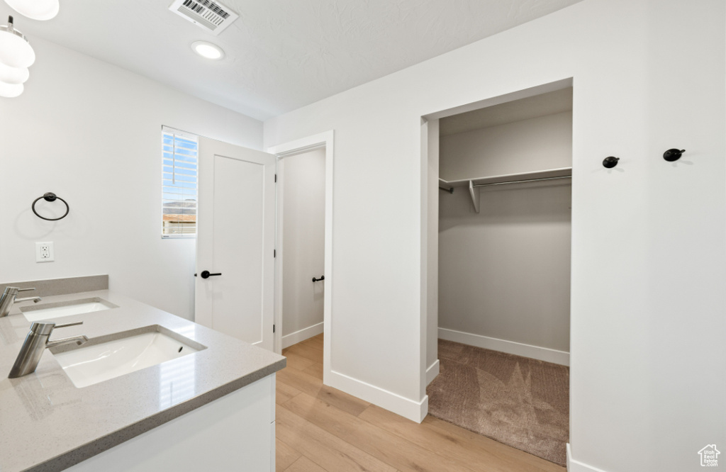 Full bath with double vanity, wood finished floors, baseboards, recessed lighting, and a spacious closet