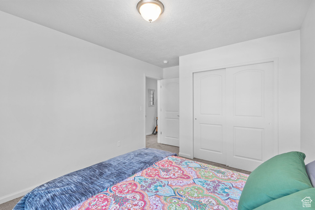 Carpeted bedroom featuring baseboards, a closet, and a textured ceiling