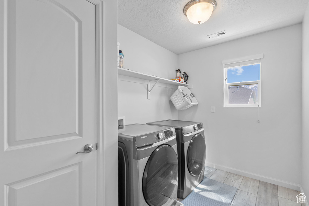 Laundry area with washer and dryer, baseboards, a textured ceiling, and wood finish floors