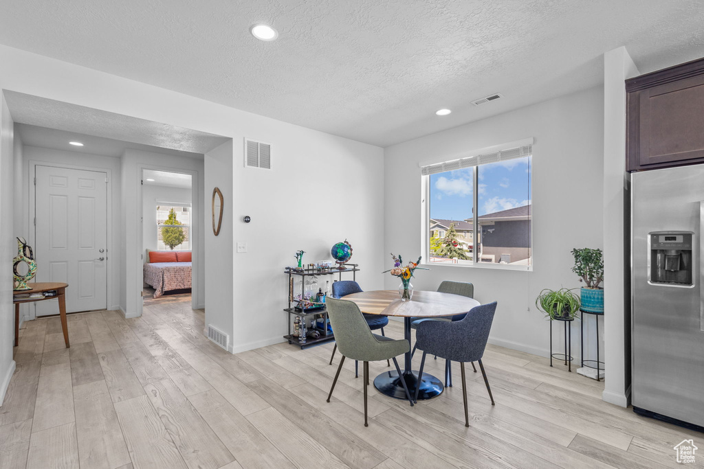 Dining space featuring light wood finished floors, a textured ceiling, recessed lighting, and baseboards