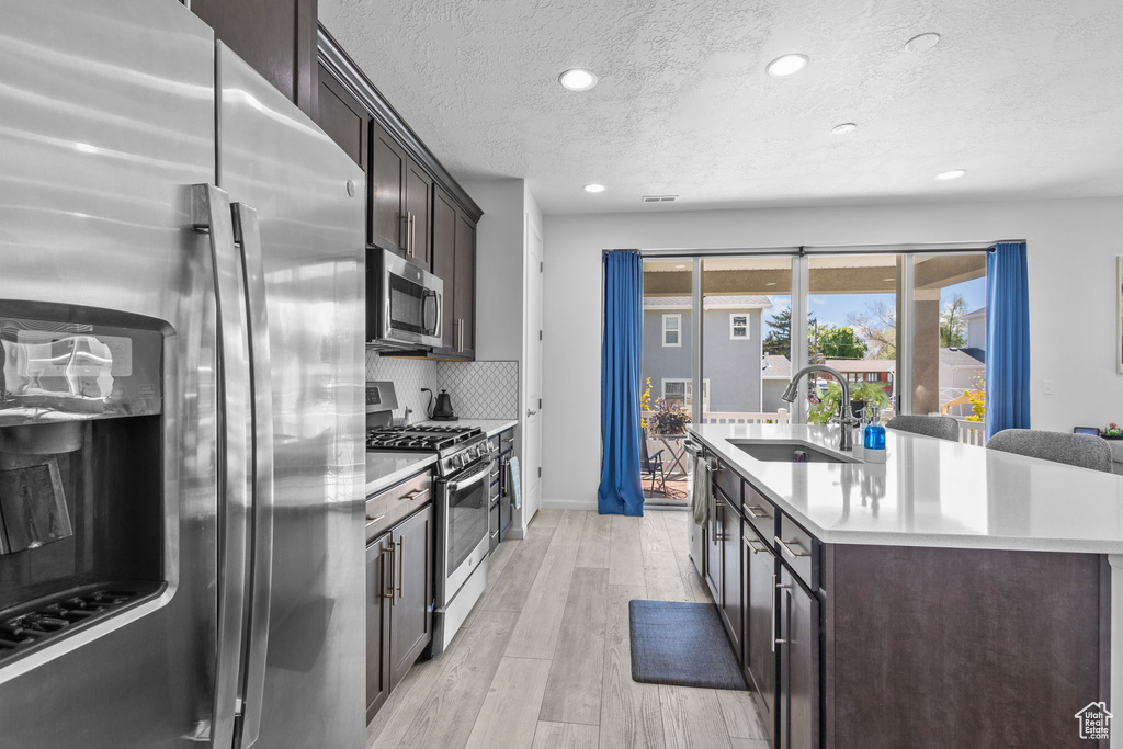 Kitchen featuring appliances with stainless steel finishes, a sink, a center island with sink, a textured ceiling, and light countertops