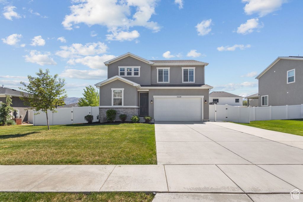 View of front of property featuring concrete driveway, stucco siding, stone siding, an attached garage, and a gate