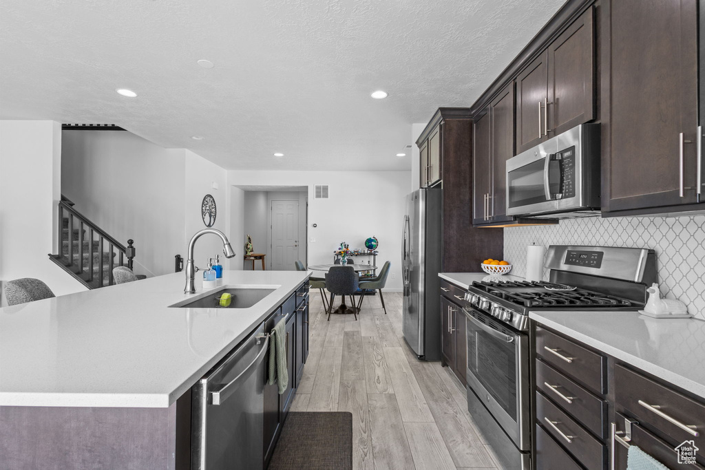 Kitchen with stainless steel appliances, a sink, light wood finished floors, light countertops, and dark brown cabinets