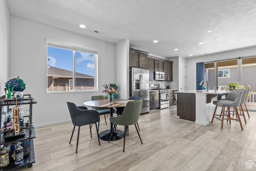 Dining space with light wood-style flooring, recessed lighting, baseboards, and a textured ceiling