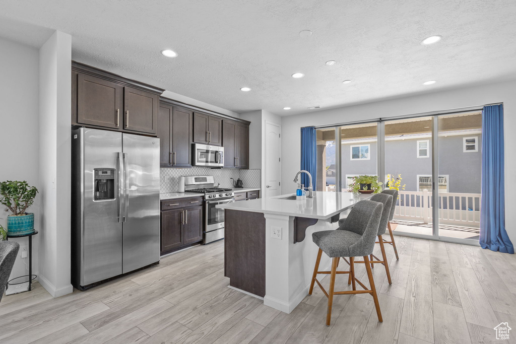 Kitchen with appliances with stainless steel finishes, a sink, dark brown cabinetry, recessed lighting, and light wood finished floors