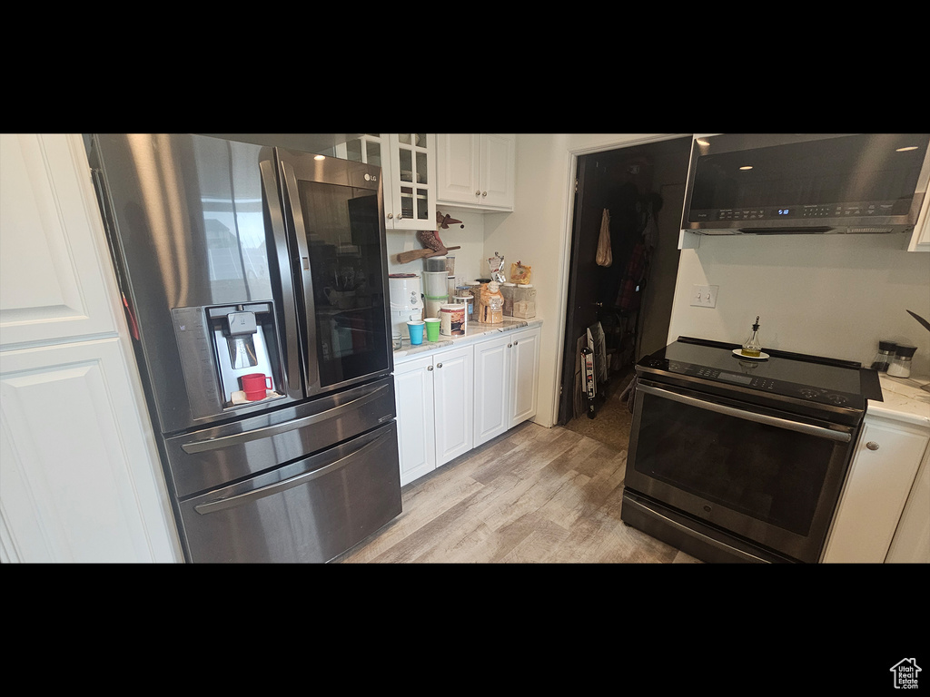 Kitchen featuring stainless steel appliances, exhaust hood, light wood finished floors, light countertops, and white cabinetry