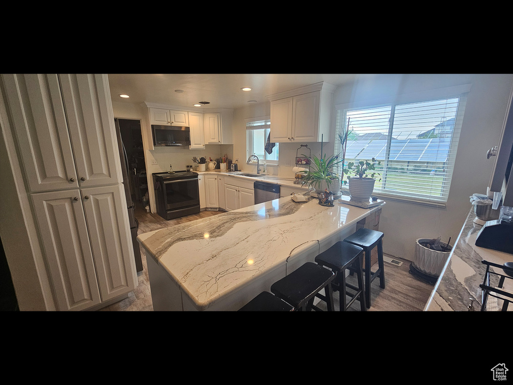 Kitchen with black range with electric stovetop, a sink, white cabinetry, light wood-style floors, and stainless steel dishwasher