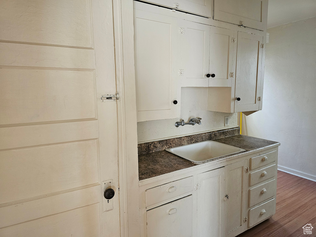 Kitchen featuring dark countertops, a sink, dark wood-type flooring, baseboards, and white cabinetry