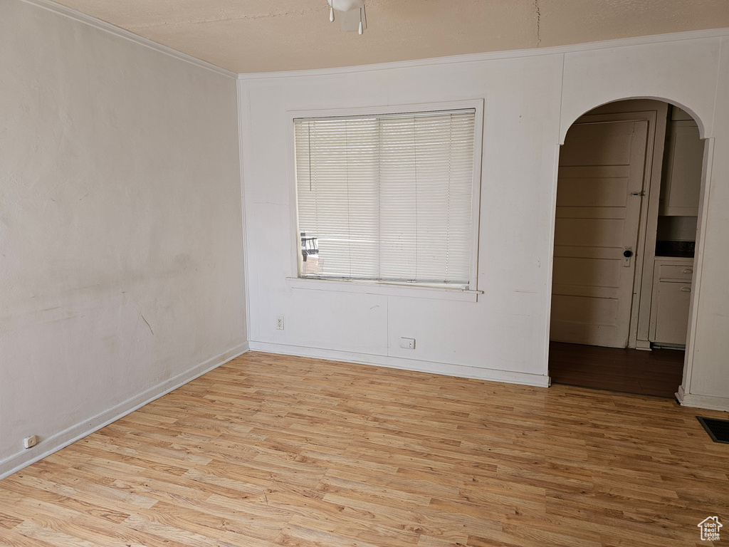 Empty room with arched walkways, light wood-style floors, baseboards, and crown molding