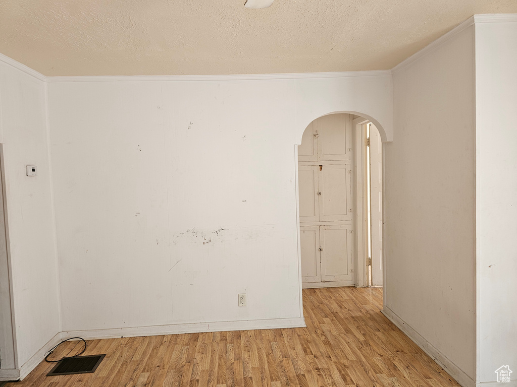 Unfurnished room featuring arched walkways, light wood finished floors, crown molding, a textured ceiling, and baseboards