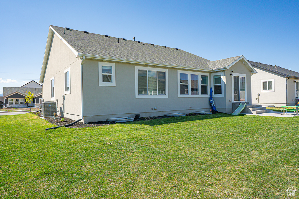 Rear view of property featuring central AC, a yard, and stucco siding