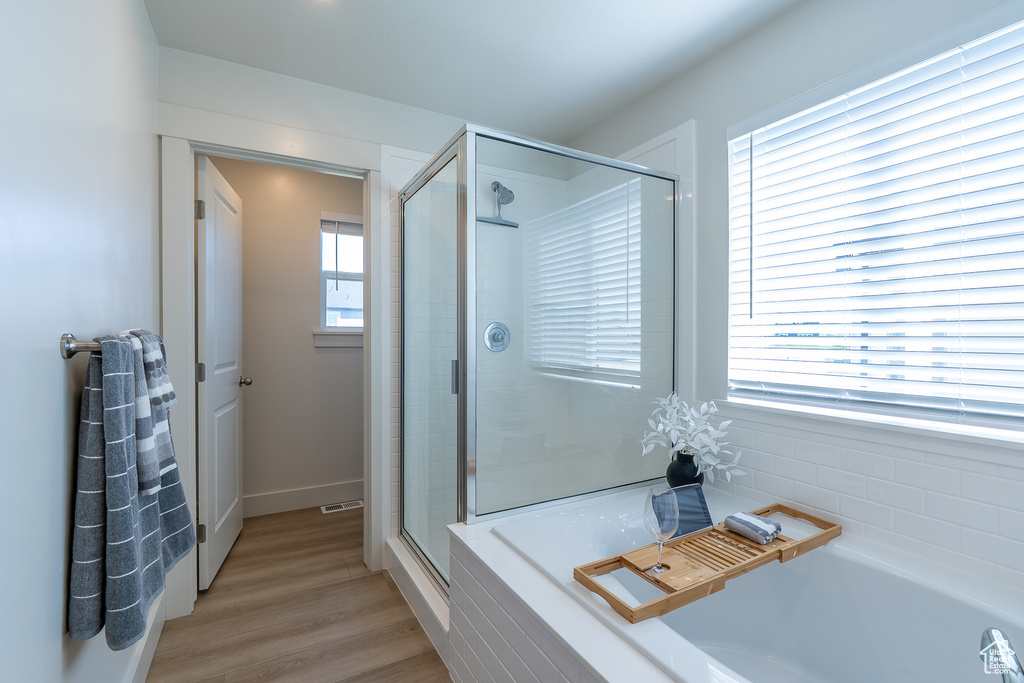 Full bath featuring a stall shower, a garden tub, wood finished floors, and baseboards