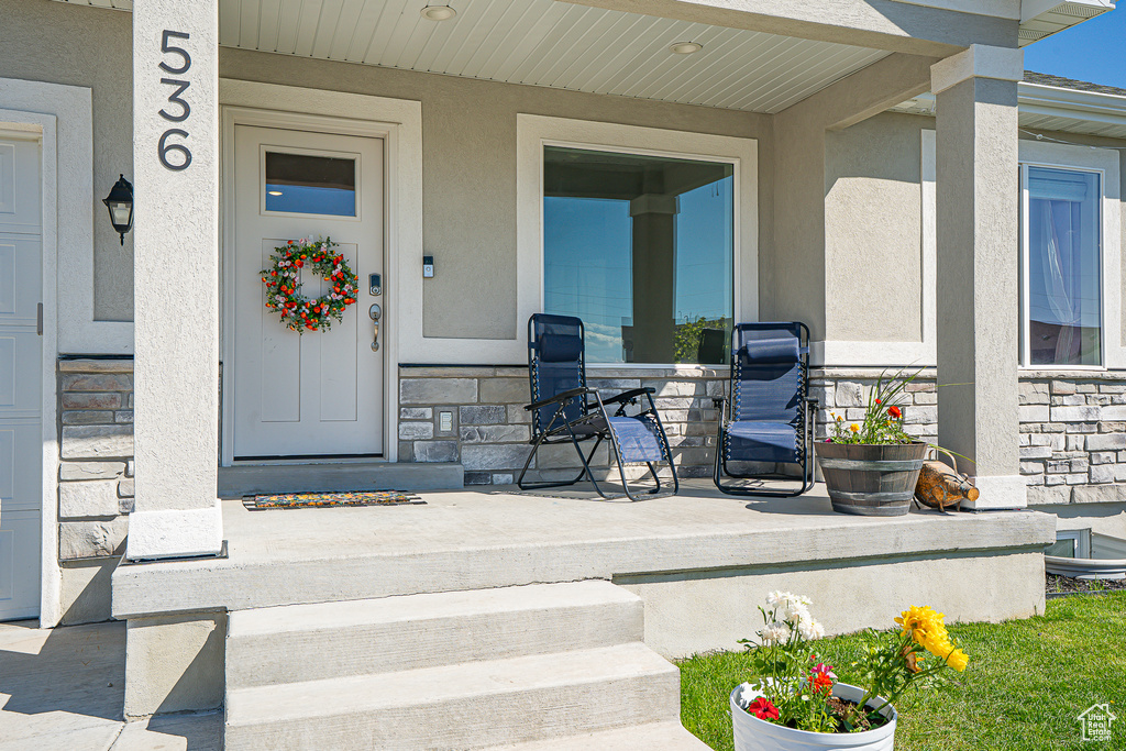Doorway to property with stone siding, stucco siding, and a porch