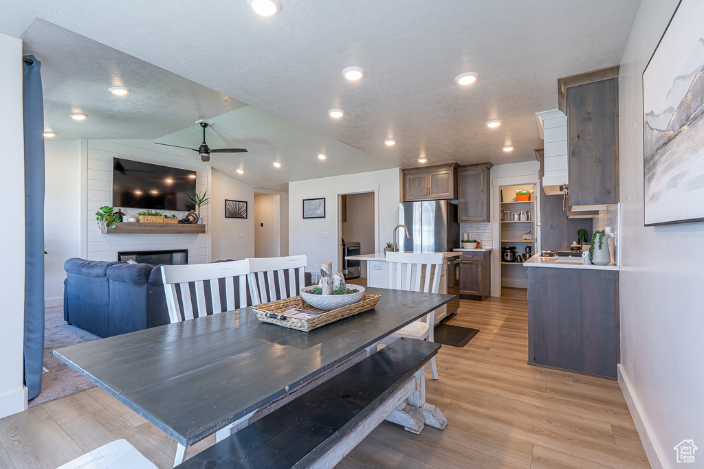 Dining space with a ceiling fan, light wood-style flooring, a fireplace, baseboards, and lofted ceiling