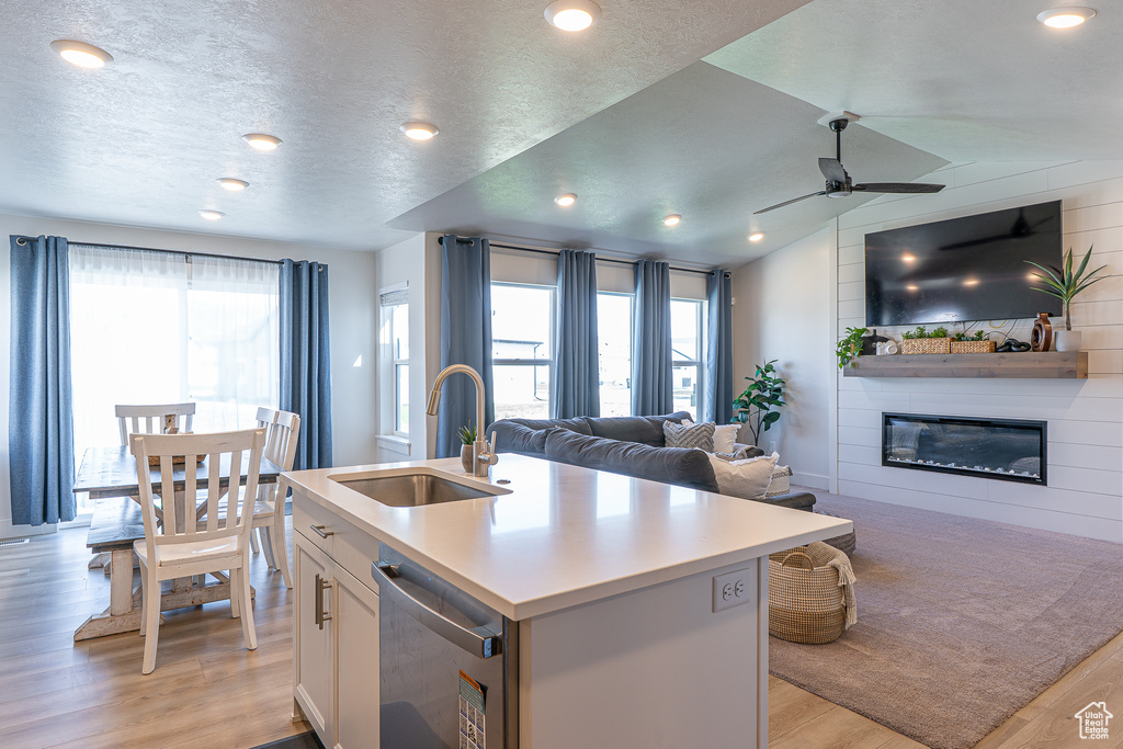 Kitchen featuring a sink, light wood-type flooring, open floor plan, ceiling fan, and a fireplace