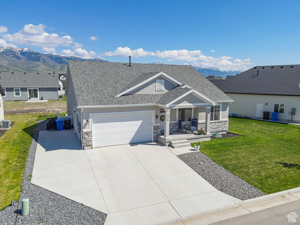 View of front of property with stone siding, a garage, roof with shingles, and a mountain view