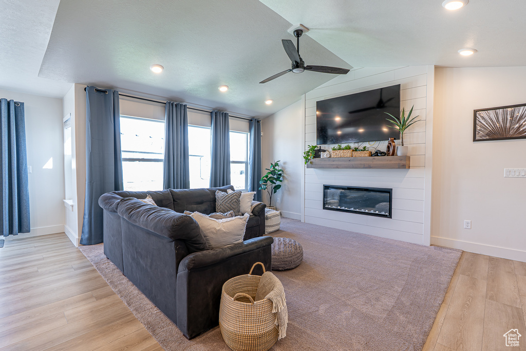 Living area featuring a ceiling fan, a fireplace, wood finished floors, baseboards, and vaulted ceiling