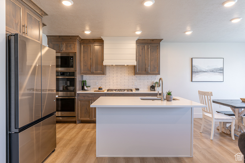 Kitchen featuring appliances with stainless steel finishes, decorative backsplash, light countertops, light wood-type flooring, and recessed lighting