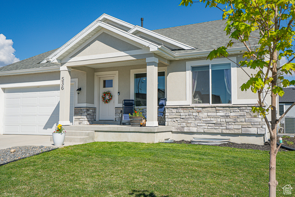 View of front facade featuring stone siding, a porch, an attached garage, a front lawn, and stucco siding