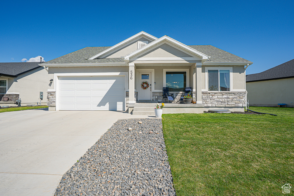 View of front of property with stone siding, covered porch, driveway, an attached garage, and a front lawn