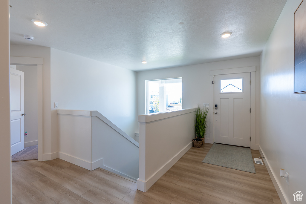 Foyer with light wood finished floors, baseboards, a textured ceiling, and recessed lighting