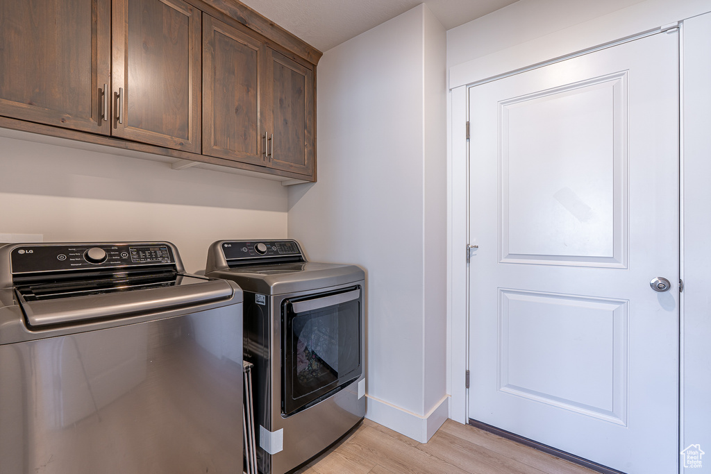Laundry room with washer and dryer, light wood-style flooring, cabinet space, and baseboards