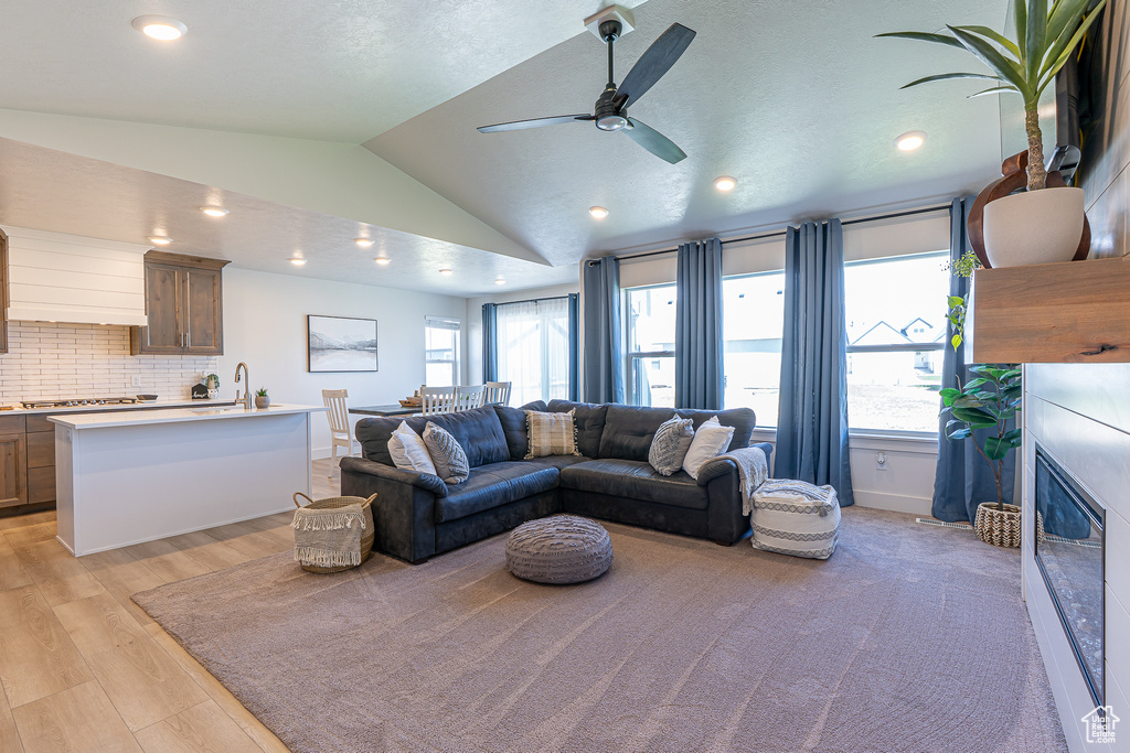 Living area featuring lofted ceiling, a ceiling fan, a glass covered fireplace, light wood-style flooring, and recessed lighting
