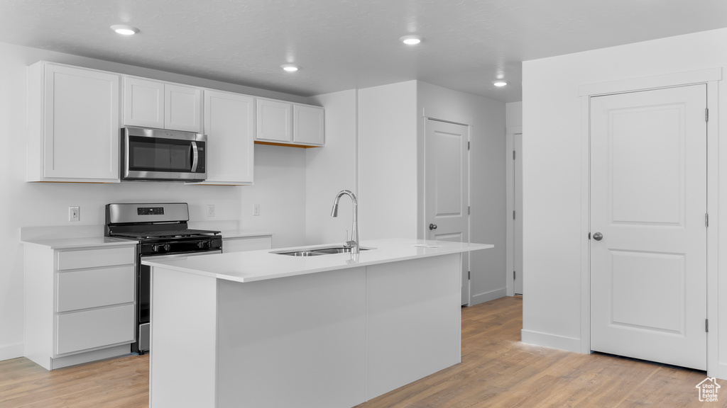 Kitchen featuring stainless steel appliances, a sink, light wood finished floors, white cabinetry, and light countertops