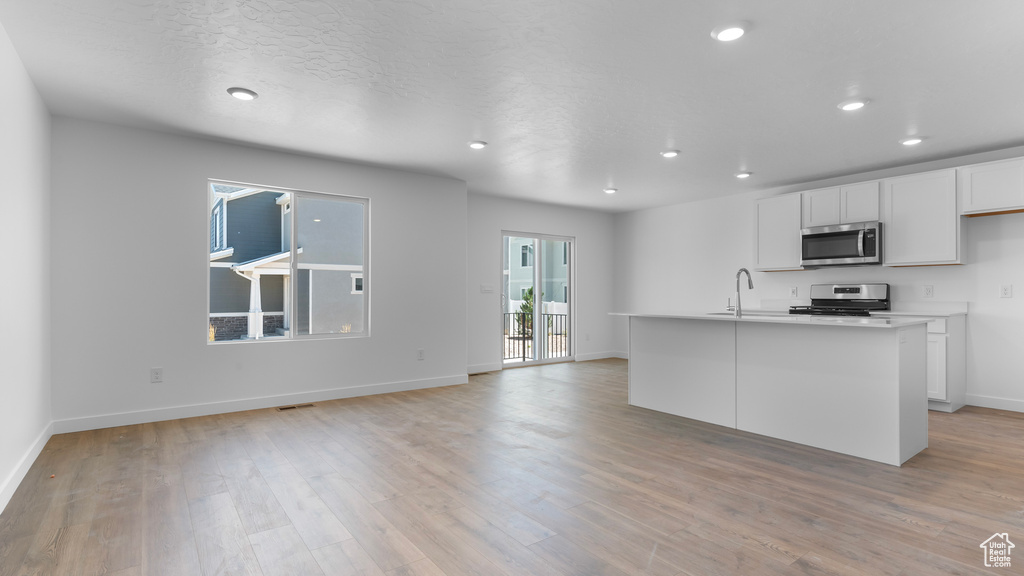 Kitchen with stainless steel appliances, a sink, light wood finished floors, recessed lighting, and white cabinetry