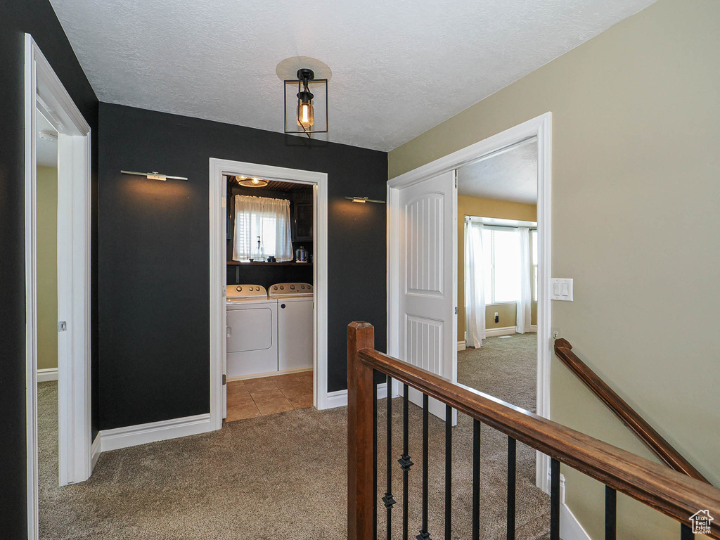 Corridor with an upstairs landing, separate washer and dryer, carpet flooring, a textured ceiling, and baseboards