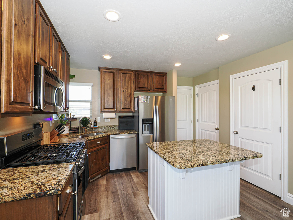 Kitchen featuring appliances with stainless steel finishes, dark wood-style flooring, a kitchen breakfast bar, a sink, and stone counters