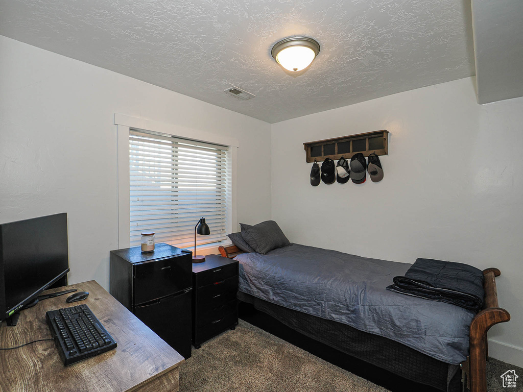 Carpeted bedroom featuring a textured ceiling and a desk
