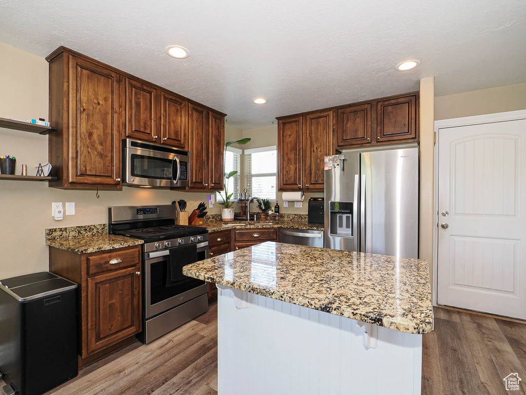Kitchen with stainless steel appliances, open shelves, wood finished floors, light stone counters, and a center island