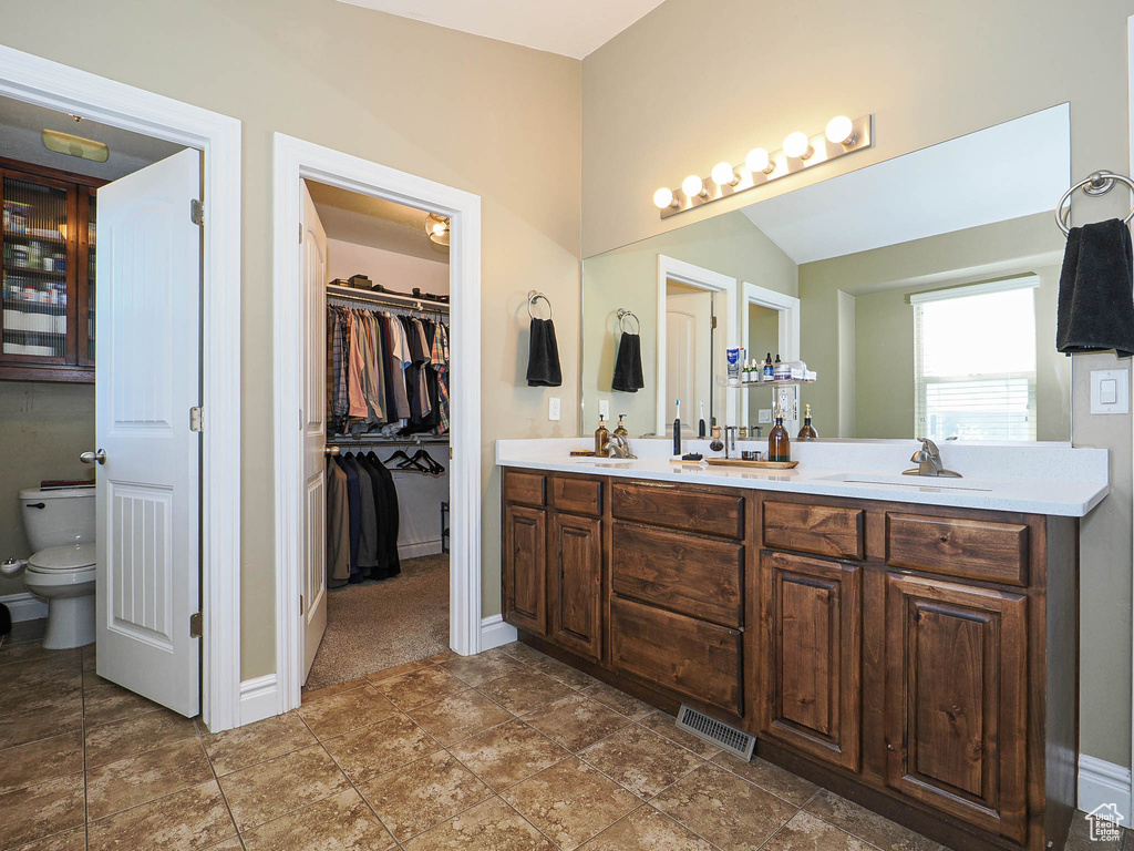 Bathroom with double vanity, baseboards, toilet, a spacious closet, and lofted ceiling