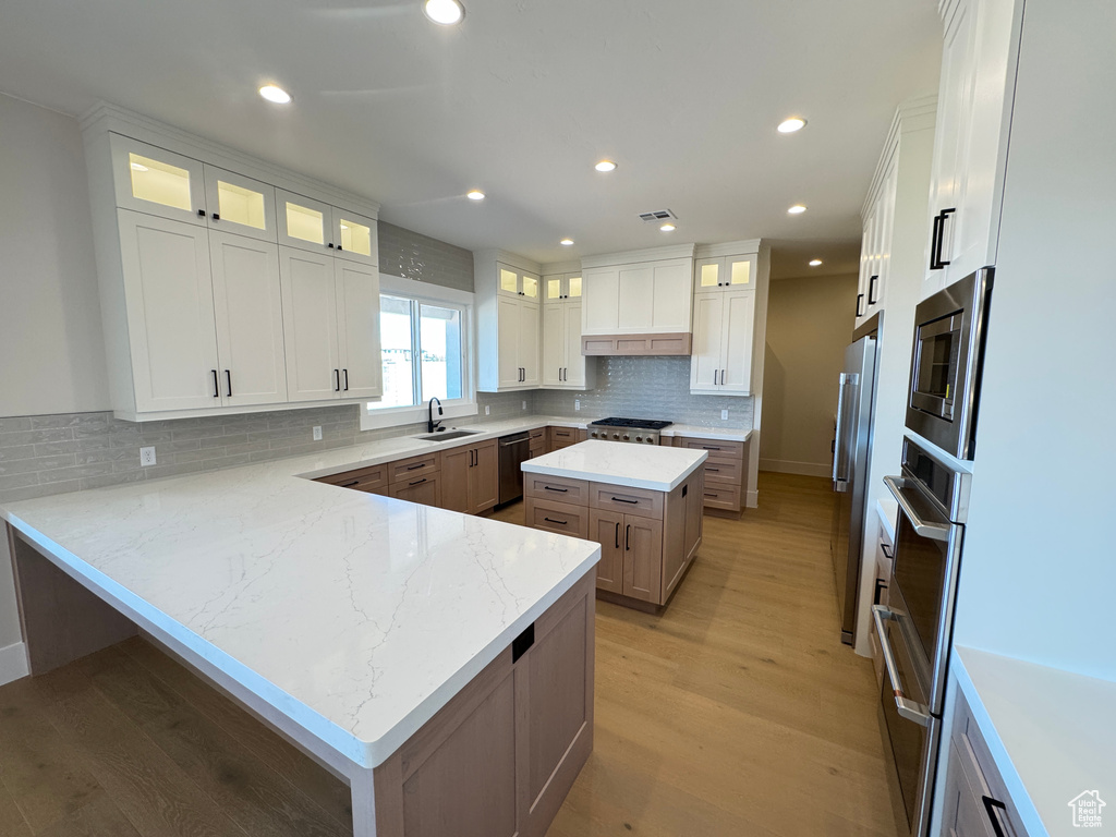 Kitchen featuring stainless steel appliances, a peninsula, backsplash, light wood-style flooring, and white cabinets