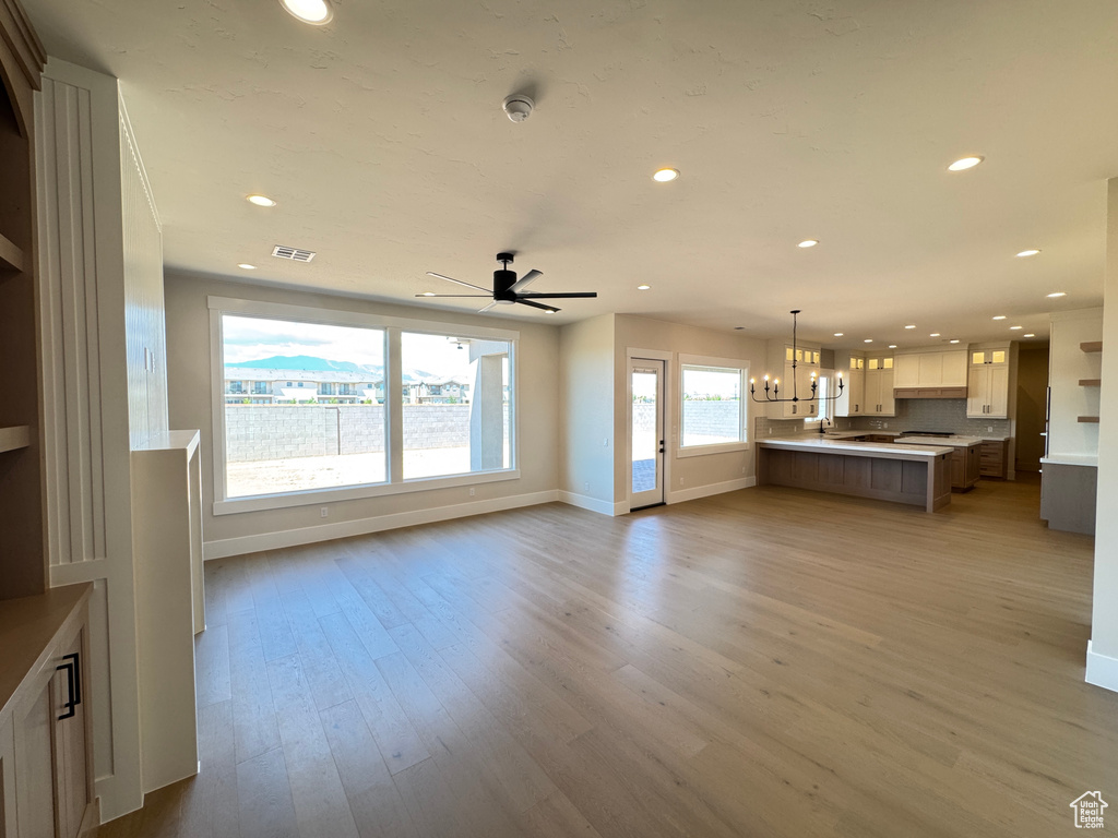 Unfurnished living room featuring recessed lighting, baseboards, a chandelier, light wood-style flooring, and a ceiling fan