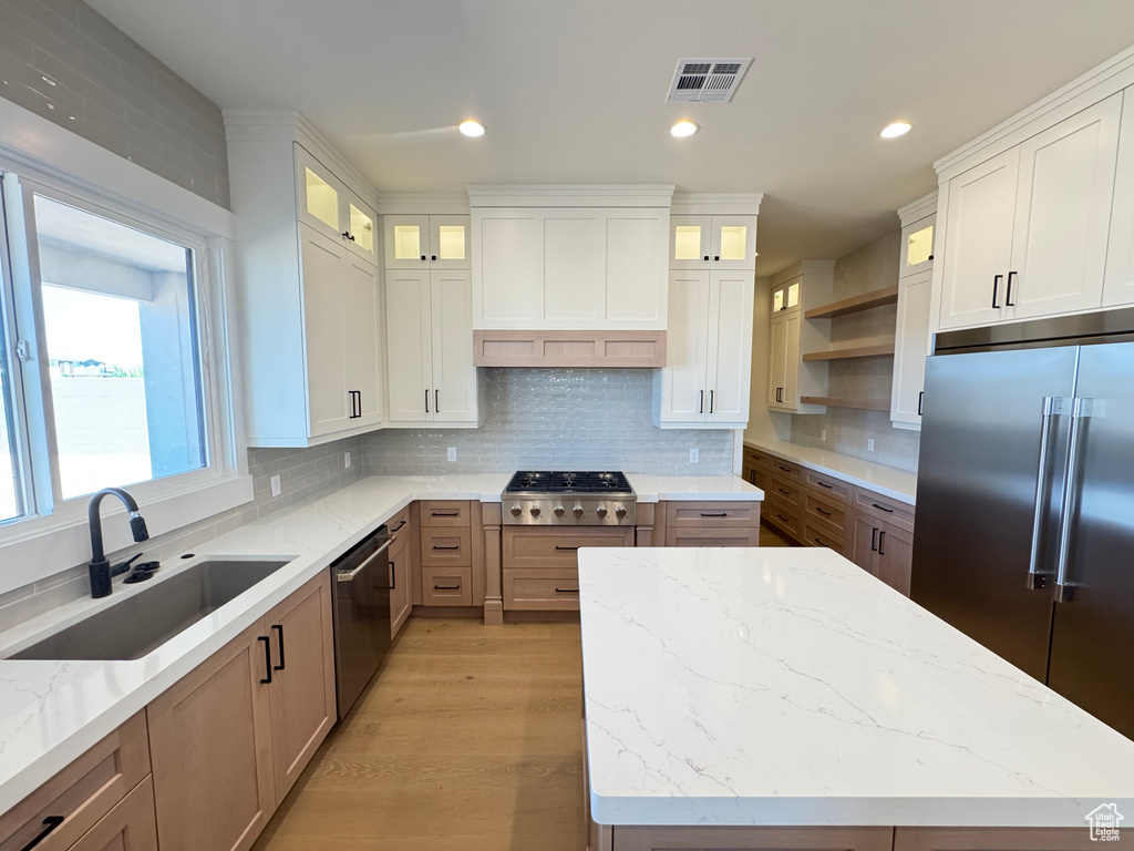 Kitchen with stainless steel appliances, a sink, open shelves, tasteful backsplash, and light stone countertops
