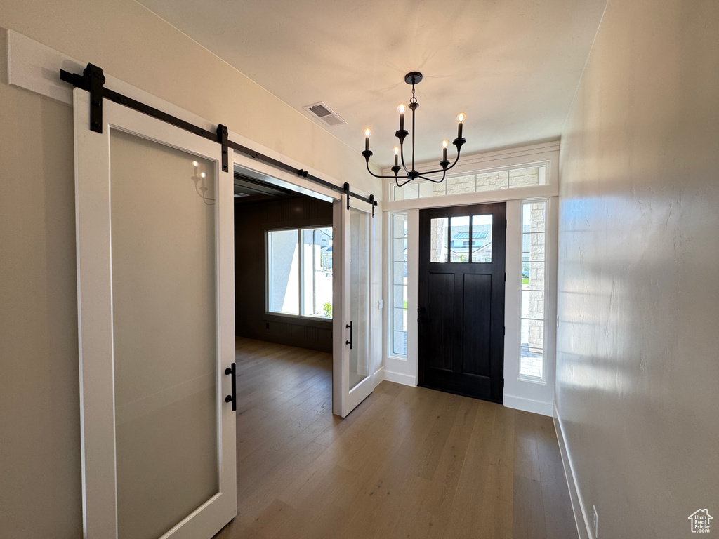 Entryway featuring a barn door, wood finished floors, a chandelier, and baseboards