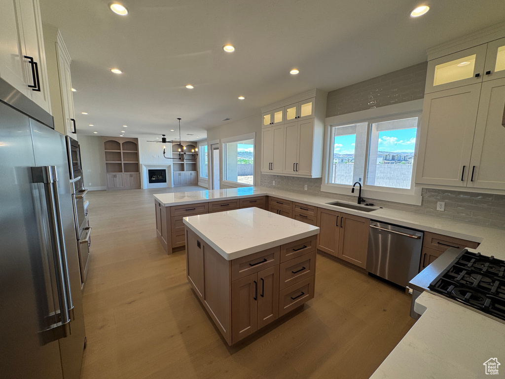Kitchen with stainless steel appliances, a sink, open floor plan, light wood finished floors, and decorative backsplash