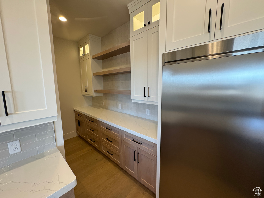 Kitchen featuring built in fridge, open shelves, light wood-style flooring, backsplash, and glass insert cabinets