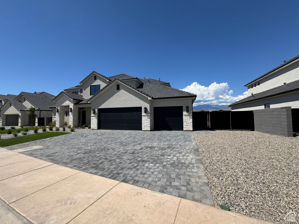 View of front of property with stone siding, a garage, decorative driveway, stucco siding, and a tiled roof