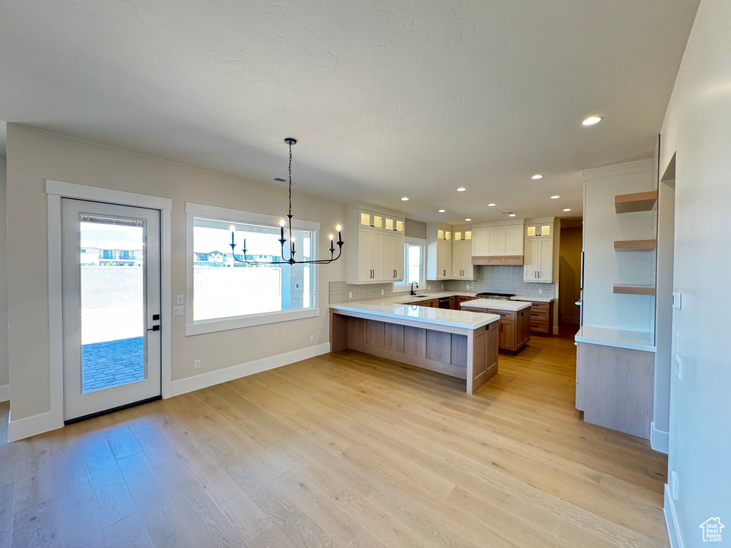 Kitchen featuring a peninsula, light wood finished floors, light countertops, glass insert cabinets, and recessed lighting