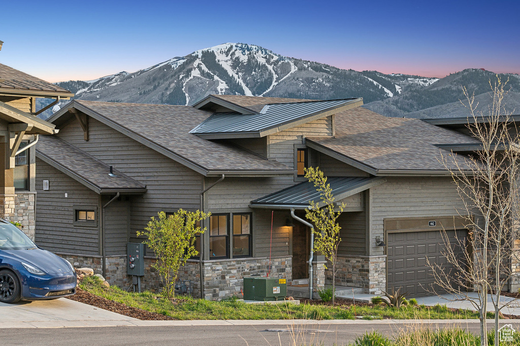 View of front of home featuring a mountain view, a garage, stone siding, and a shingled roof