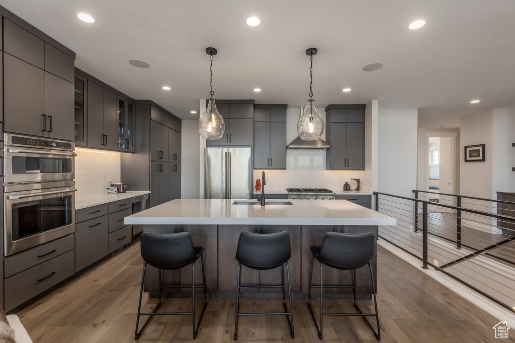 Kitchen with appliances with stainless steel finishes, a sink, a breakfast bar area, light countertops, and light wood-style floors