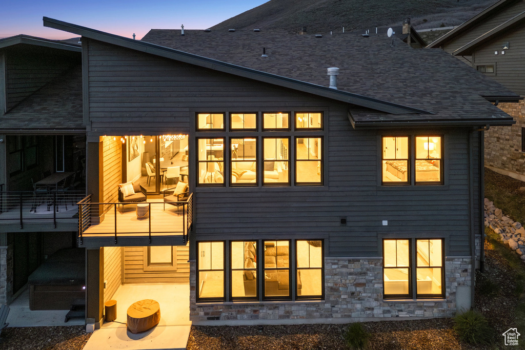 Back of house at dusk featuring a balcony, stone siding, and a patio