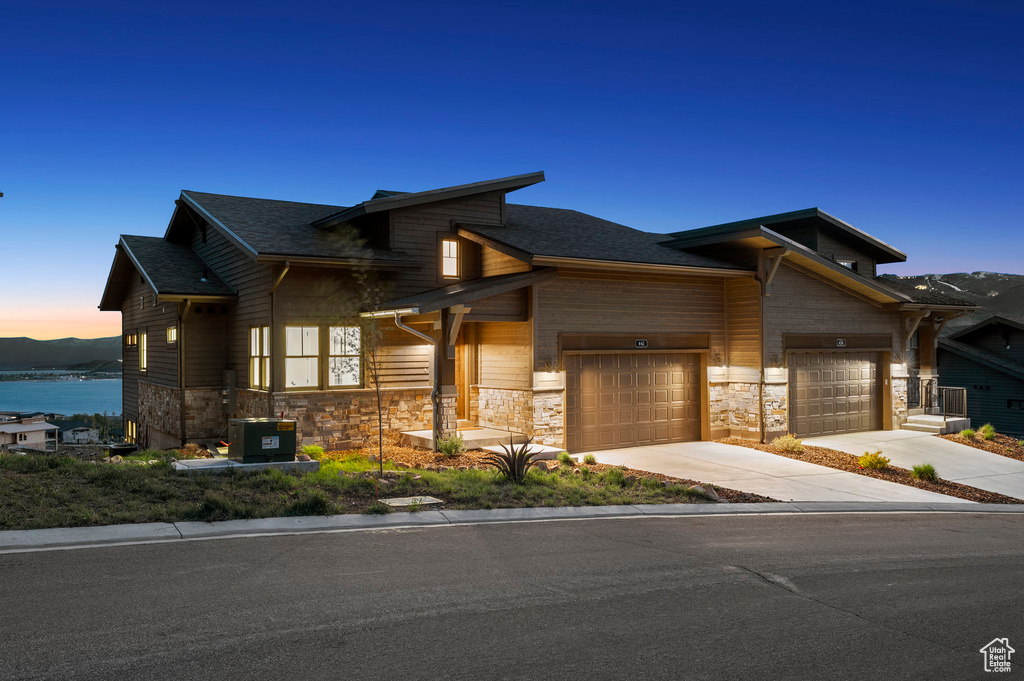 View of front of house featuring driveway, stone siding, a garage, cooling unit, and a shingled roof