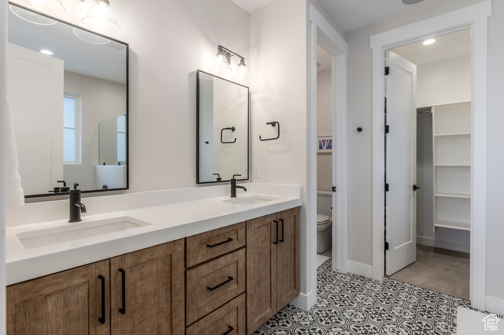 Full bath with toilet, a walk in closet, and double vanity